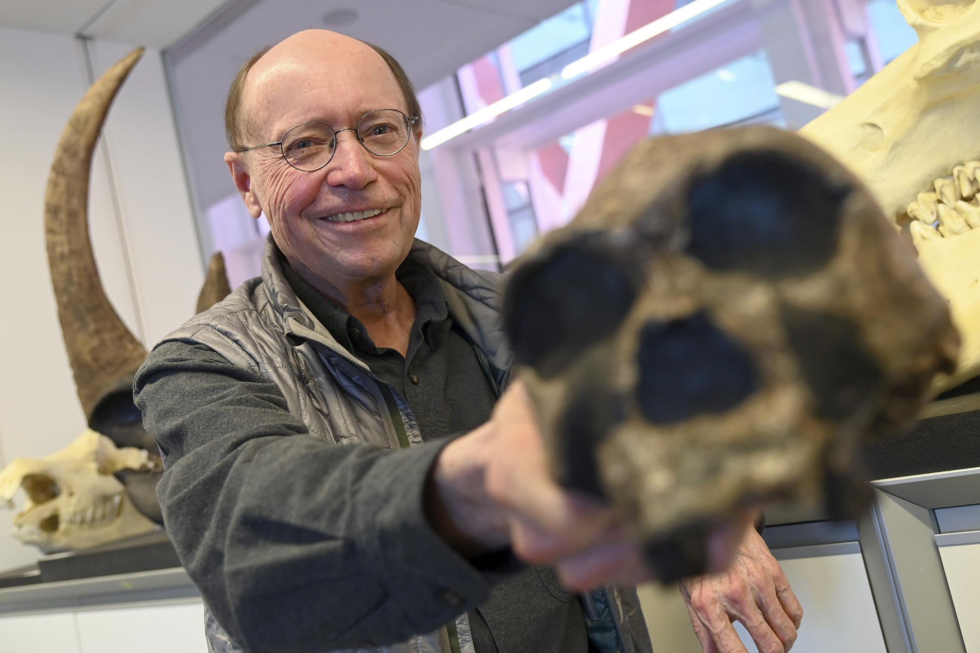 A man holds a hominid skull up to the camera.